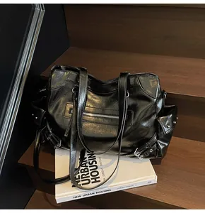 High-angle view of black glossy leather commuter tote bag with metallic buckle details.