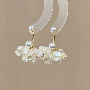 Close-up detail of elegant pearl petal earrings with golden hardware on a display stand.