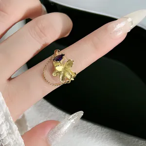 Detalle de un anillo de flor dorada con gema púrpura y borla de cadena delicada.