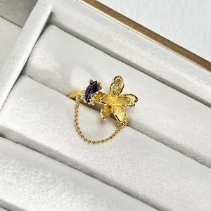 Primer plano detallado de un anillo de flor dorada con gema púrpura y cadena fina.