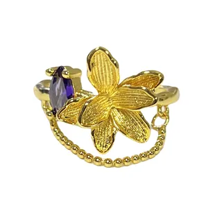 Vista detallada del anillo de flor dorada con piedra púrpura y cadena de perlas.