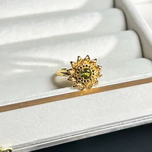Detailaufnahme eines goldenen Sonnenblumenrings mit funkelndem grünem Edelsteinzentrum