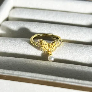 Detailansicht eines goldenen Schmetterlingsrings mit Perlenanhänger und Steinen