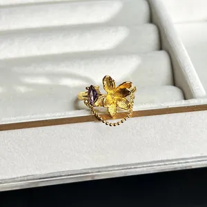 Nahaufnahme eines goldenen 3D-Blumenrings mit violettem Stein und feiner Perlenkette