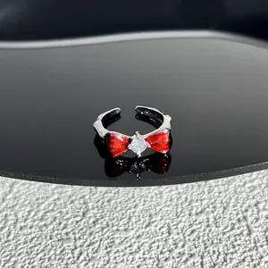 Détail macro d'une bague argentée avec un nœud rouge et un cristal central étincelant