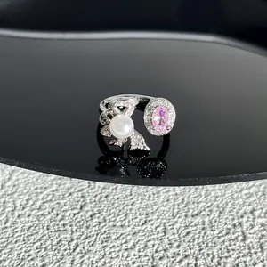 Détail d'une bague nœud argentée ornée d'une perle blanche et d'un joyau rose ovale.