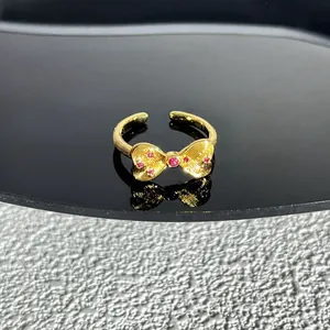 Gros plan d'une bague nœud dorée avec pierres roses sur une surface noire miroir.