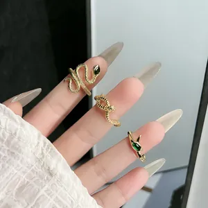 Detailed view of golden snake-shaped rings with green gemstones on manicured fingers.