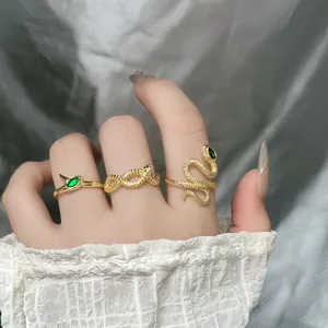 Detailed view of golden snake wrap open rings with green gemstones on a model's hand.