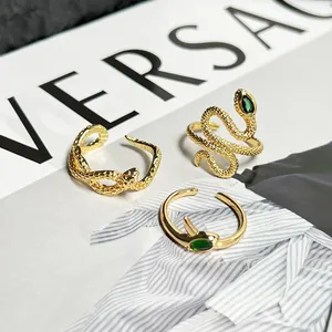 Close-up macro view of three gold-plated snake-shaped open rings with green stones