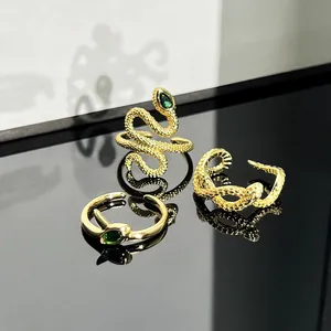 Close-up of three golden snake-shaped open rings with green gemstone accents.