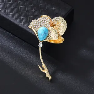 Close-up detail of luxury gold ginkgo leaf brooch featuring a blue turquoise stone