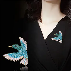 Detailansicht einer stilvollen blauen Kolibri-Brosche an schwarzer Kleidung gesteckt.