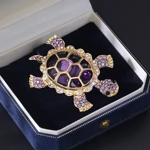 Detailed view of a gold-plated purple turtle brooch with sparkling rhinestones in a gift box