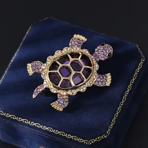Detailed view of turtle brooch featuring purple rhinestones and glass on a blue velvet box
