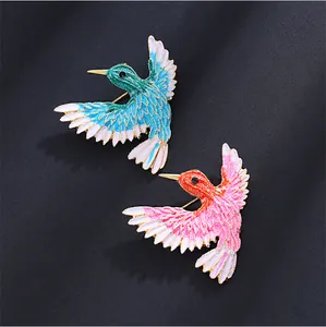 Detailansicht von zwei glitzernden Kolibri-Broschen in leuchtendem Blau und Pink