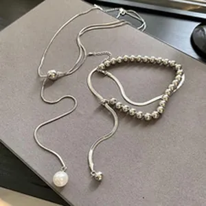 Detail of silver snake chain necklace with pearl and bead accents on grey background