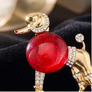 Élégante broche caniche dorée avec corps en résine rouge et strass brillants.