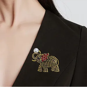Detailweergave van een gouden olifantenbroche met rode strassteentjes en een parel.