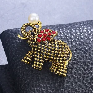 Detailopname van een vintage olifantbroche met rode strass en een grote witte parel.