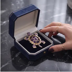 Luxury gold-tone turtle brooch featuring purple crystals presented in a blue velvet gift box