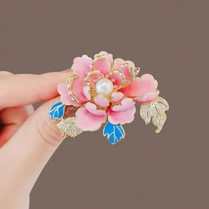 Close-up detail of a pink enamel peony brooch with a central pearl and blue leaves.