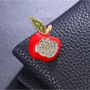 Detailed macro view of a red enamel apple brooch decorated with glittering green rhinestones.