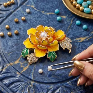 Elegant yellow enamel peony flower brooch with a central pearl and sparkling green leaves