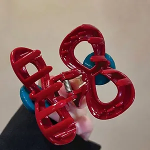 Macro view of the elegant red bow-shaped hair claw clip with distinct blue button details