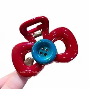 Vibrant red bow-shaped hair claw clip with a blue button center on white background.