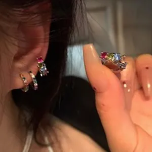 Vue macro de petites créoles en strass multicolores portées sur une oreille féminine