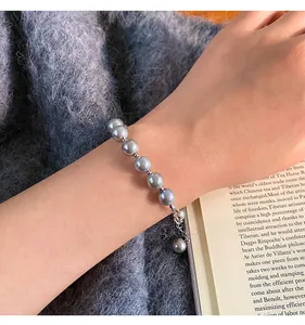 Elegant grey glass pearl bracelet with silver-tone chain worn on a wrist with a book background