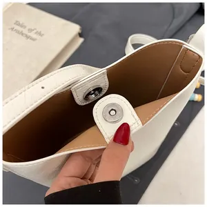 Close-up of magnetic snap closure and brown interior of stylish white bucket bag.