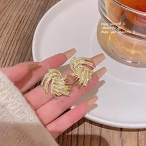 Detailed view of elegant gold-toned swirl textured earrings held by a hand.