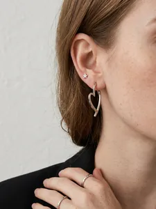 Close-up of minimalist silver heart-shaped crossover earrings worn on model's ear