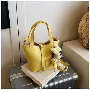 Detailed view of yellow pebble leather bucket bag featuring a cute plush puppy charm