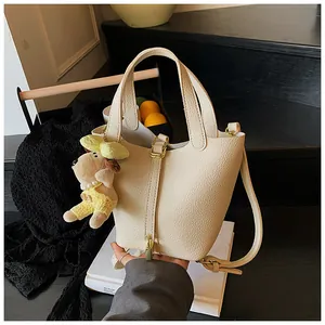 Macro view of a cream pebbled leather bucket bag featuring a cute plush dog charm