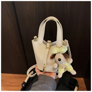 Detail of a cream pebbled leather bucket bag with a cute dog plush keychain accessory