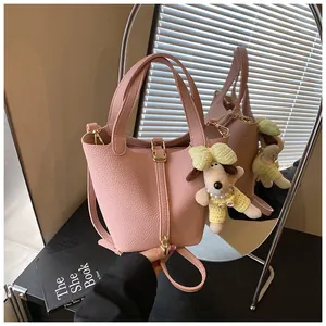 Detail of pink pebbled leather bucket bag featuring a cute plush dog charm and gold hardware