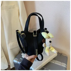 Detail view of black lychee grain leather bucket bag with cute dog charm on suitcase