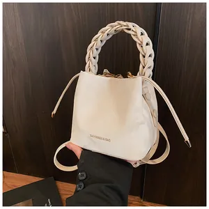 Detail view of an elegant cream bucket bag with a unique braided top handle design.