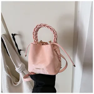 Detailed view of a stylish pink bucket bag with a braided handle and gold logo