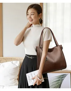 Stylish woman model carrying a large brown leather shoulder bag in a bright modern room.