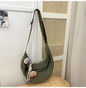 Sac bandoulière en nylon vert foncé en forme de croissant avec breloques sur porte en rotin.
