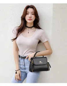 Close-up of a stylish black leather handbag with gold kangaroo logo held by a model