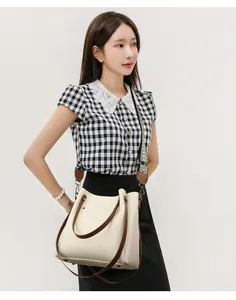 Bolso de mano de cuero crema con correa ancha geométrica lucido por una modelo.