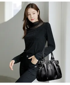 Elegante bolso de mano de piel granulada negra con logotipo de canguro en una modelo.