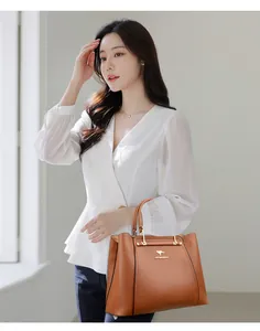 Bolso de mano de cuero marrón sostenido por mujer con blusa blanca elegante