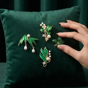 Elegante grüne Pflanzen-Emaille-Broschen mit Perlen auf einem Samtkissen