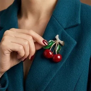 Elegant red enamel cherry brooch with rhinestone details on a teal blazer jacket